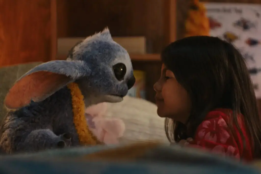 Cena do filme live-action de Lilo & Stitch mostrando Lilo ao lado de Stitch na praia, representando o laço de família e amizade da história